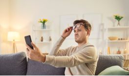 This is a man who has raised his left hand, holding a mobile phone, while his right hand is touching his glasses